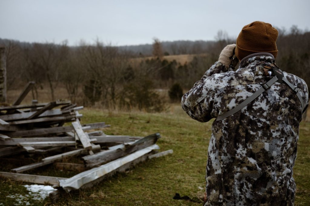 Chasseur en tenue camouflage observant un paysage boisé aux jumelles