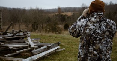 Chasseur en tenue camouflage observant un paysage boisé aux jumelles