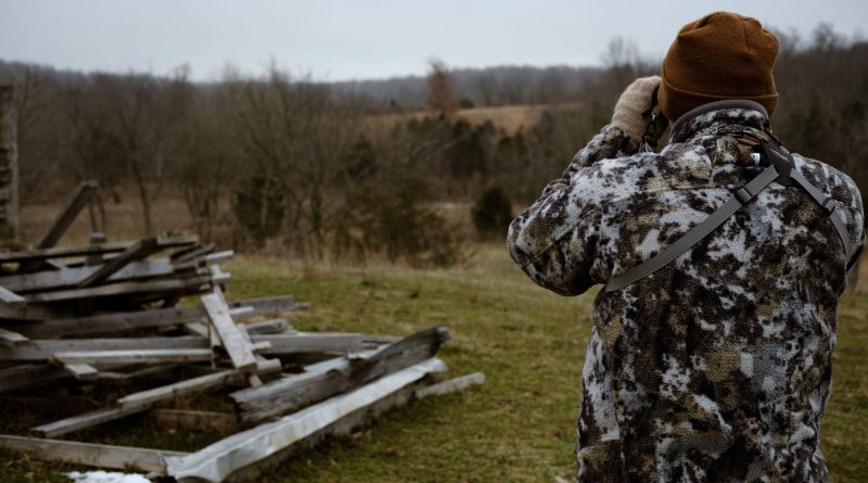 Chasseur en tenue camouflage observant un paysage boisé aux jumelles