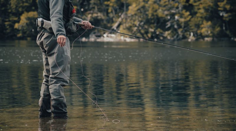 Pêcheur en waders lançant sa ligne dans une rivière calme